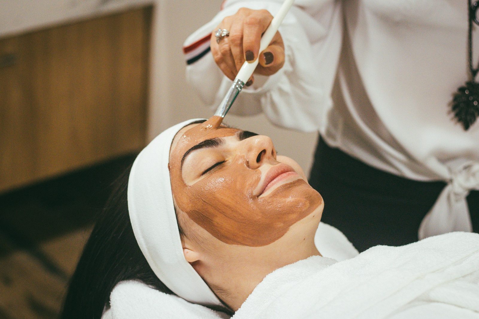 Estetista che applica una maschera viso all'argilla con pennello a una cliente in cabina